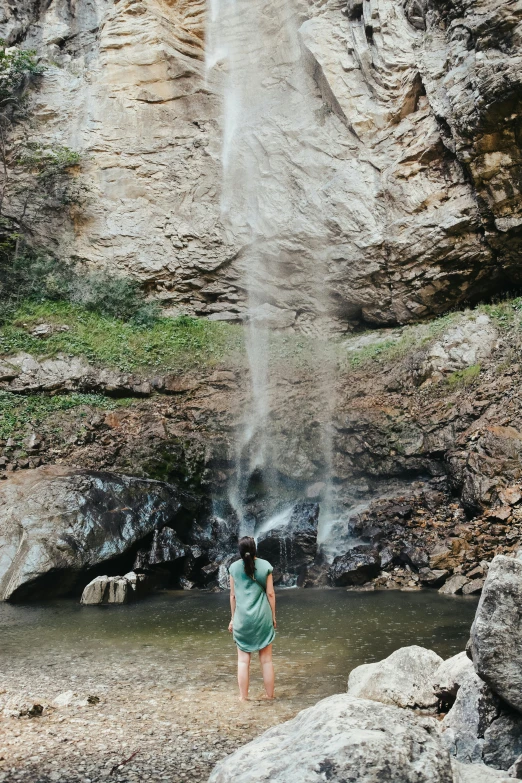 a woman standing in front of a waterfall with a water fall running down the side of it