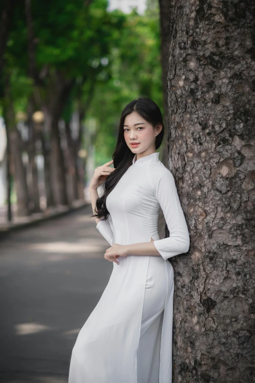 an asian woman in white poses beside a tree