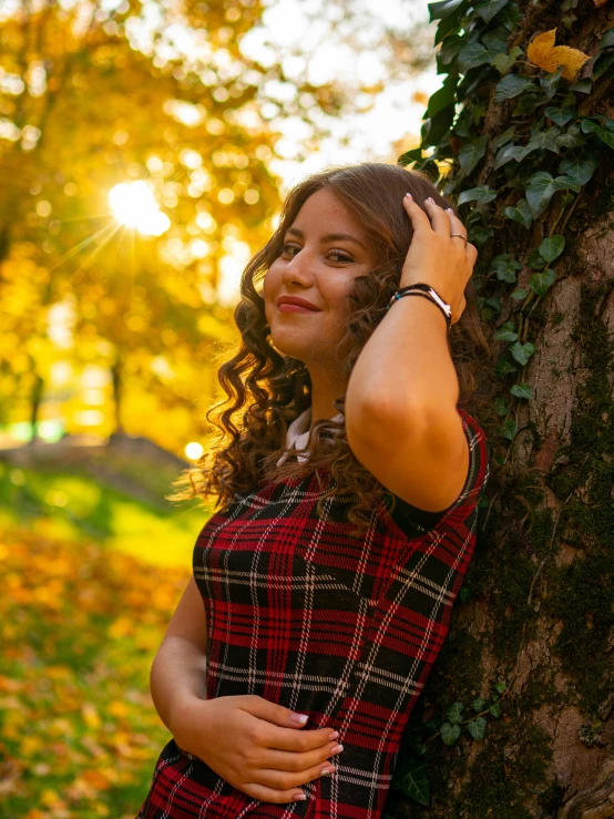 a girl standing in front of a tree with her arm around the tree