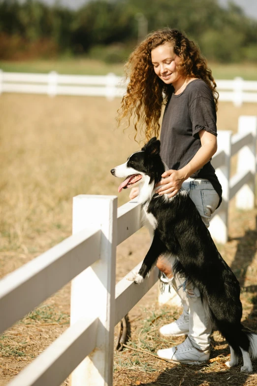 a woman poses with a dog standing next to a fence
