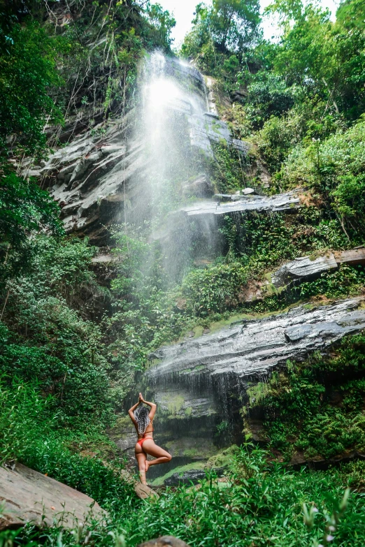 the woman in a red bikini is by a waterfall