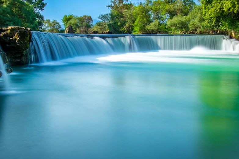 a waterfall with blue green water at the bottom and a person in a boat near it