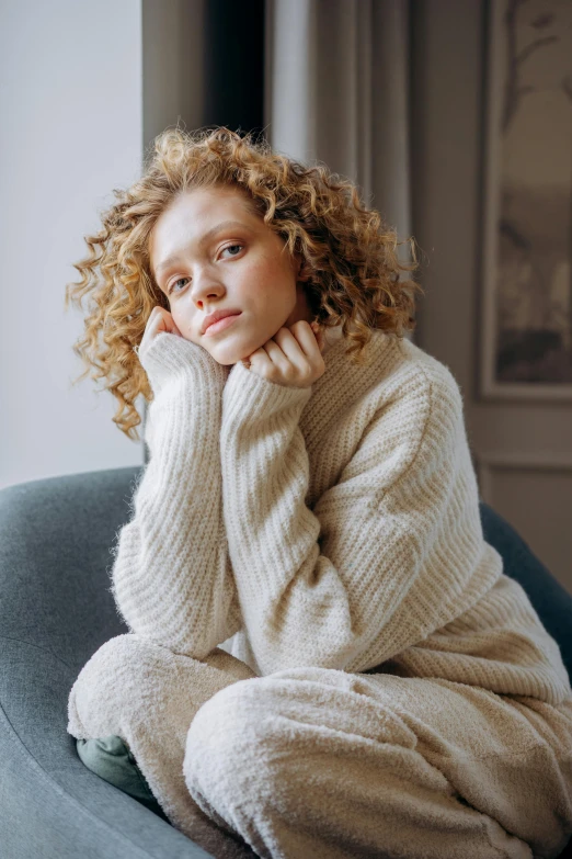 a young woman sitting on a blue sofa wearing an oversize sweater and leg warmer