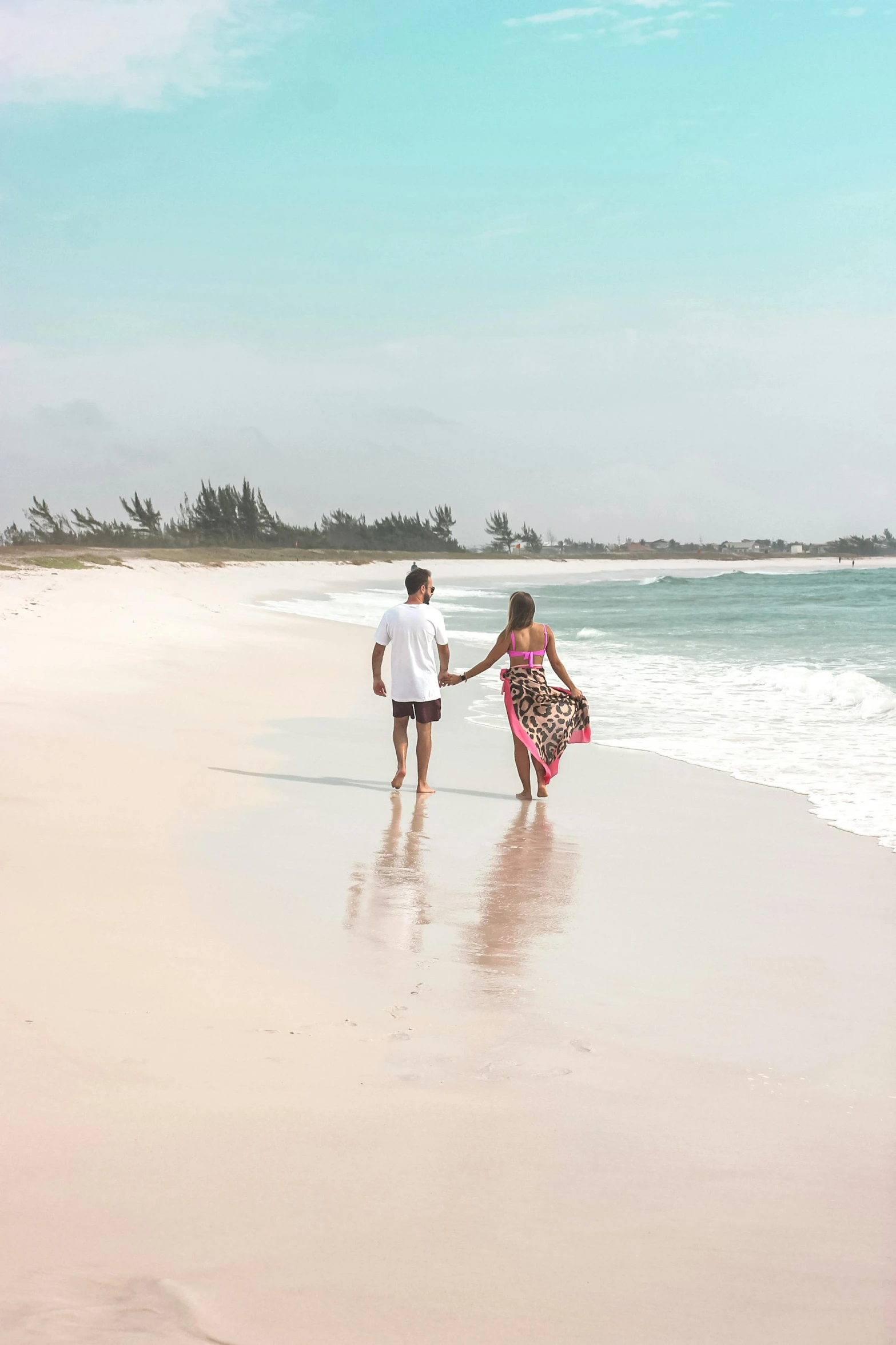 two people walking on the beach with a board