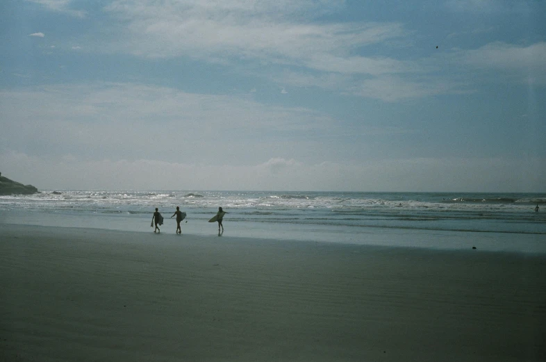 three people standing on top of the sand next to the ocean