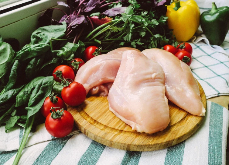 two raw chicken  on a  board surrounded by green vegetables