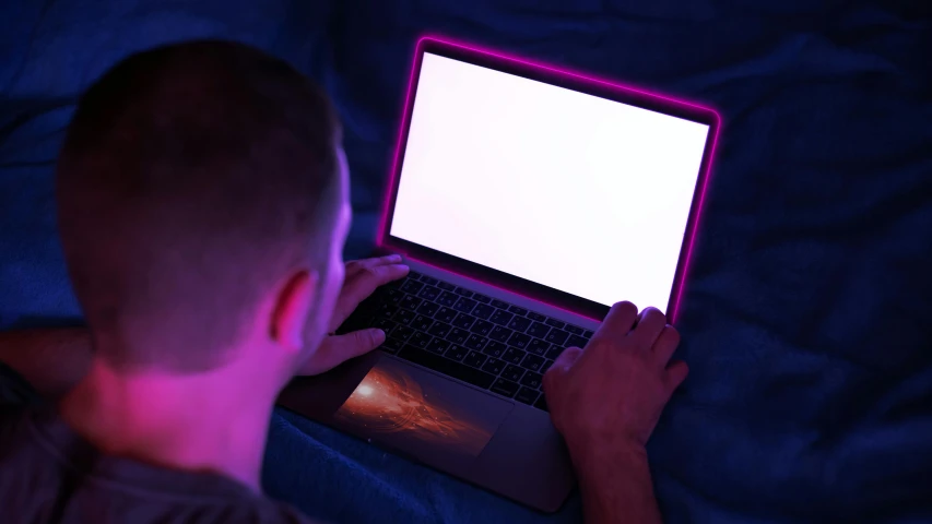 a man sitting on his bed and using a laptop with a white screen