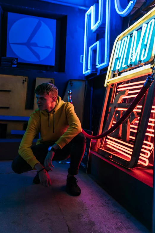 man kneeling on floor next to neon sign