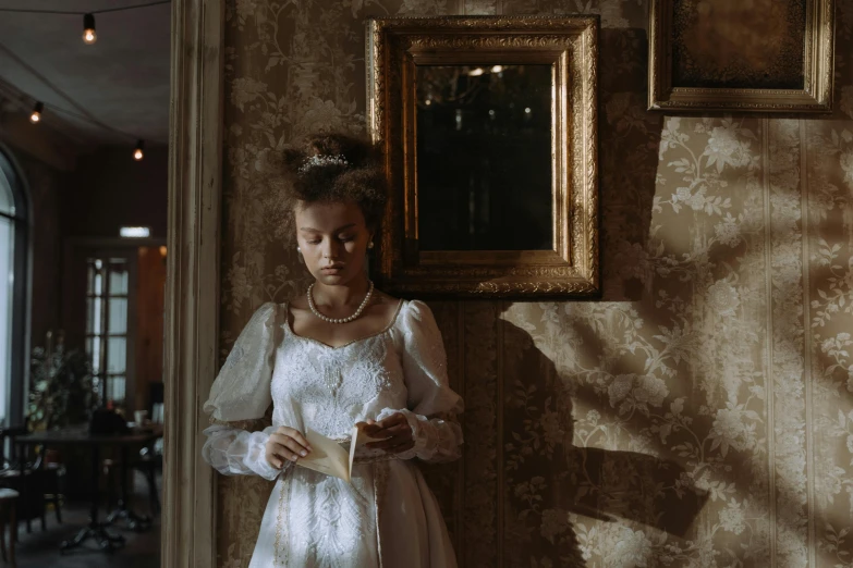 woman in dress next to framed portrait and wall with ornate decor