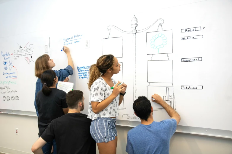 three people stand next to a whiteboard with blue marker diagrams