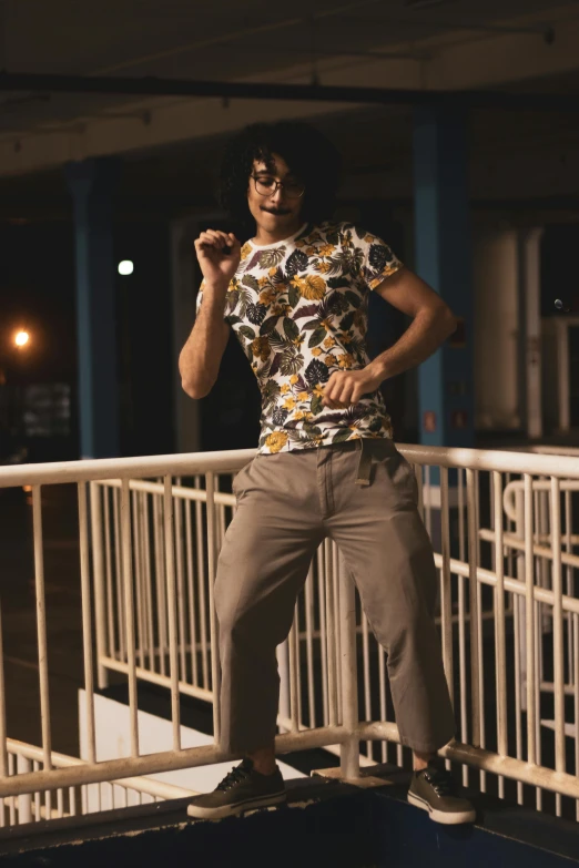 a man wearing gray pants and a flower shirt poses on a skateboard