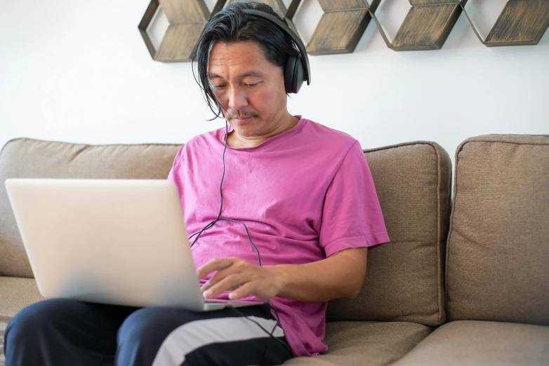 a man in headphones using his laptop on the couch