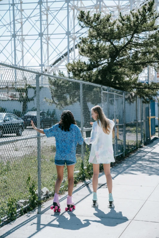 two women standing near a fence and one has skateboards