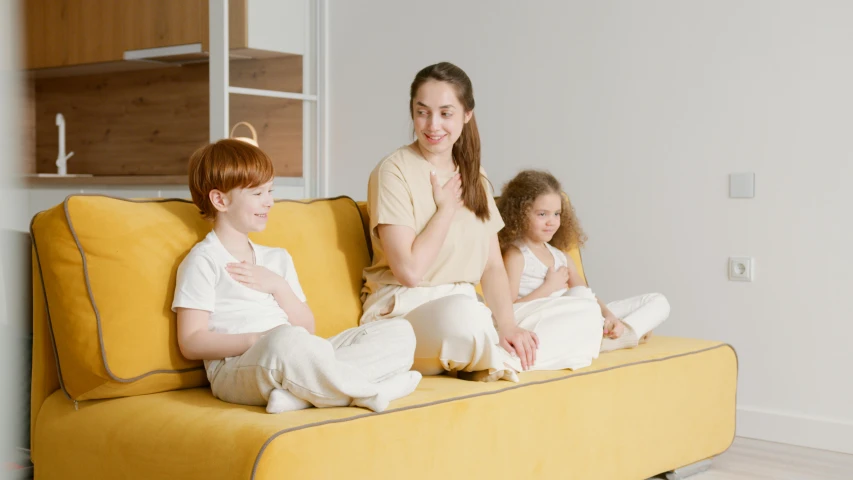 a woman in a beige shirt sitting on a yellow couch with three children