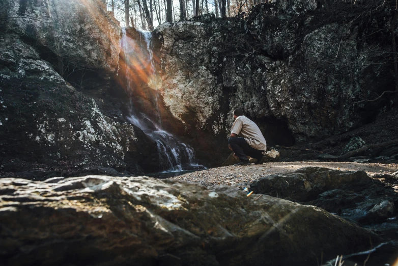 a person kneeling down near rocks next to a small waterfall