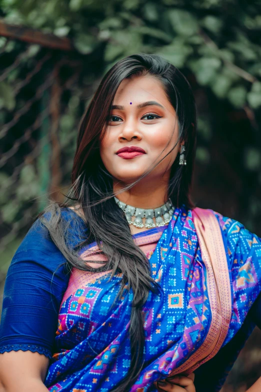 a woman standing next to some trees wearing a blue outfit