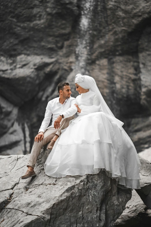 man and woman wearing white in the rain on rocks next to waterfall