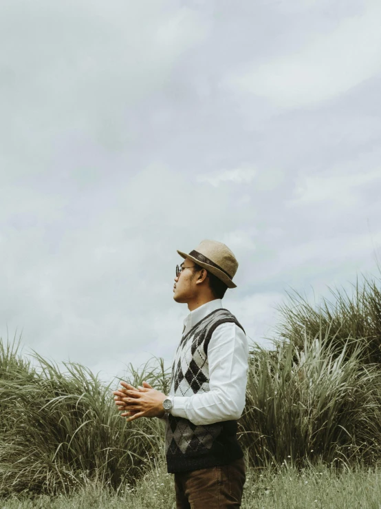 a young man standing in the grass with his hat back