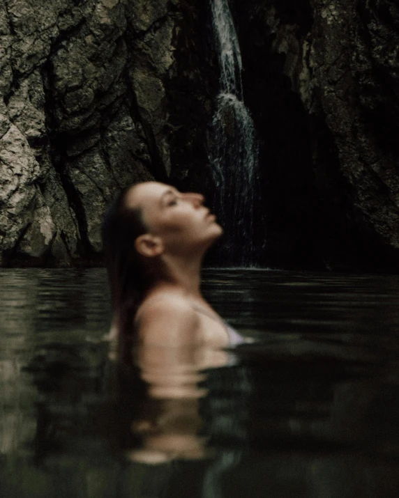 a woman swimming in a body of water with a waterfall nearby