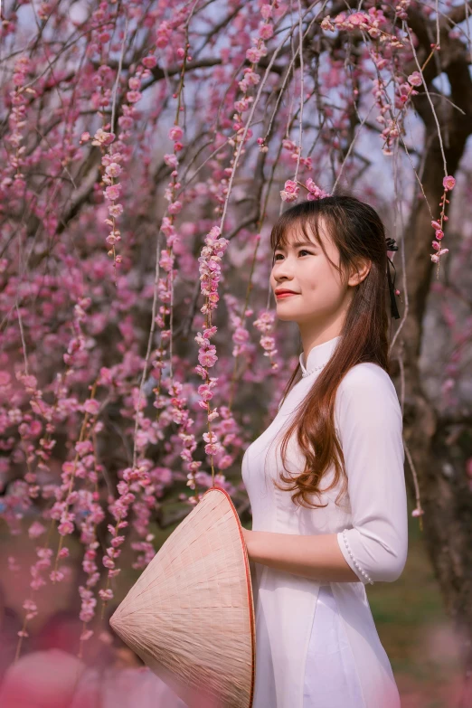 a woman holds a basket standing in front of a tree full of flowers