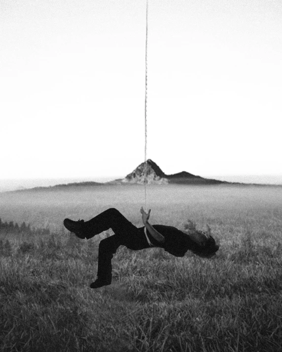 black and white pograph of a man lying on a rope