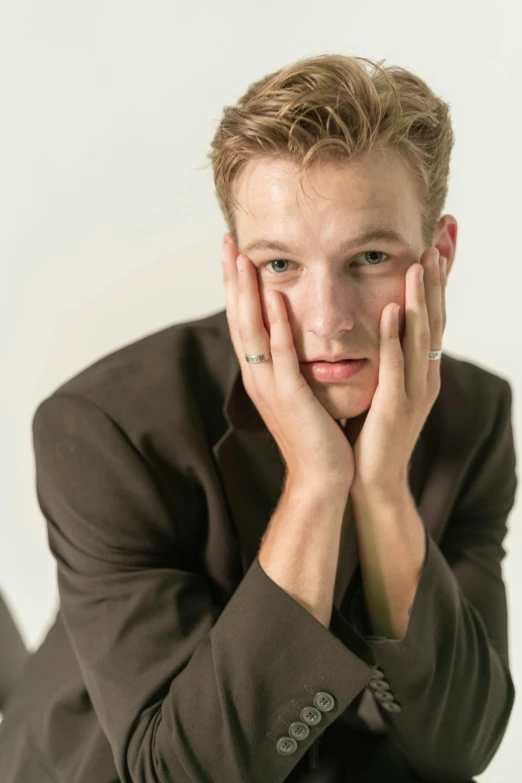 a young man sitting at a desk with his hands resting on his face