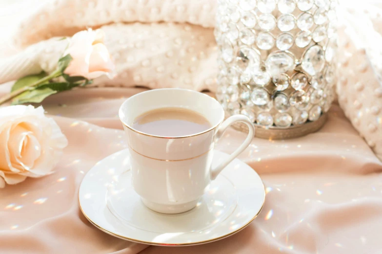 white coffee cup with saucer on pink tablecloth and white rose