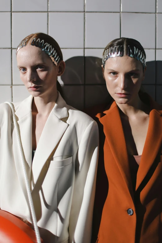 two models with matching hair clips pose in front of a tiled wall