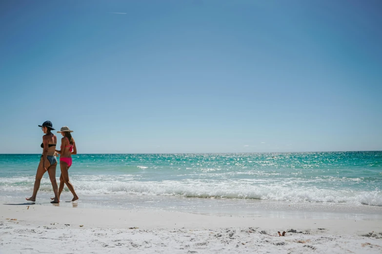 two women in bikinis walking along a beach