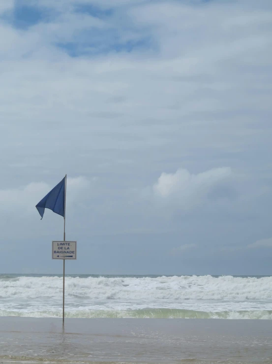 a sign on a pole sticking out from the sand next to water