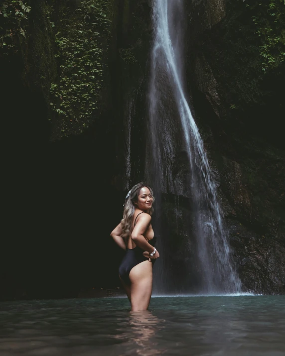 a young lady standing in the water below a waterfall