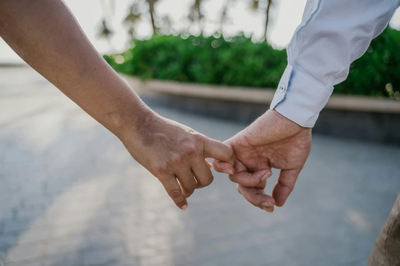 two people holding hands walking on pavement