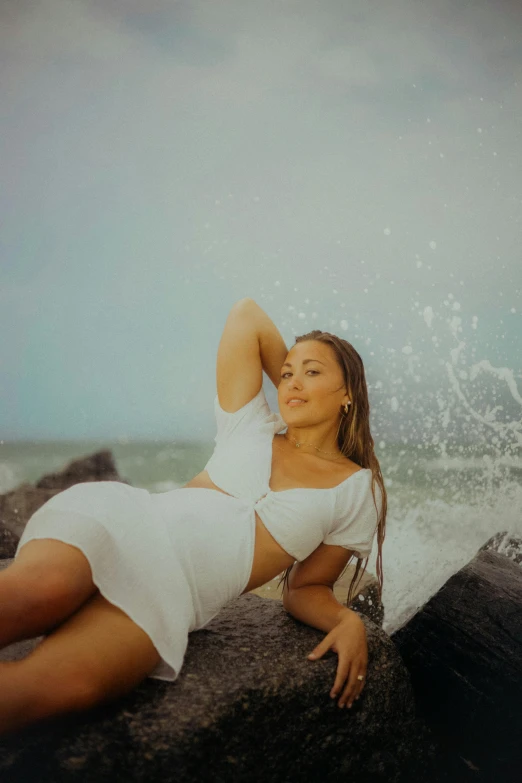 a beautiful woman in white on the rocks in front of some water