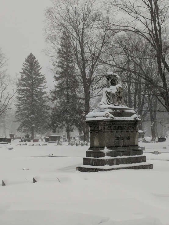 the snow covered cemetery has a statue sitting in it