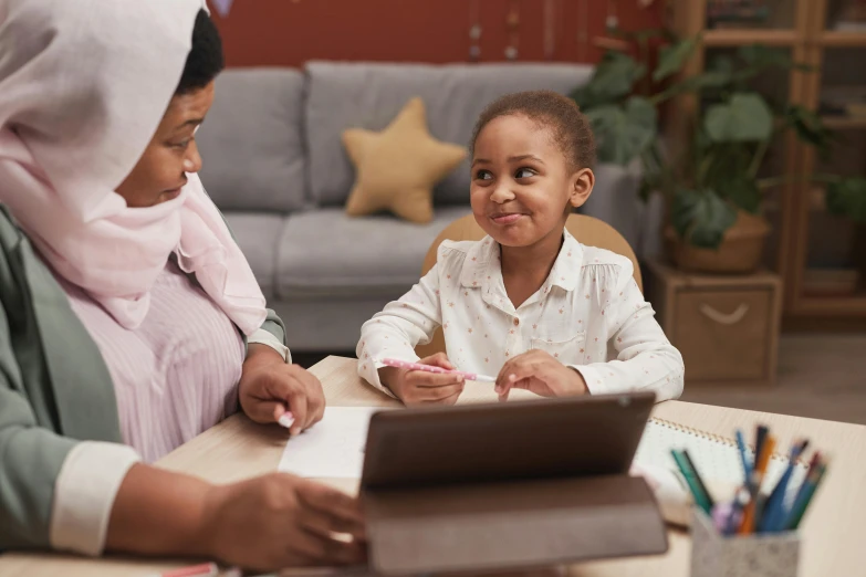 a young child sitting at a table while an older woman is using a laptop