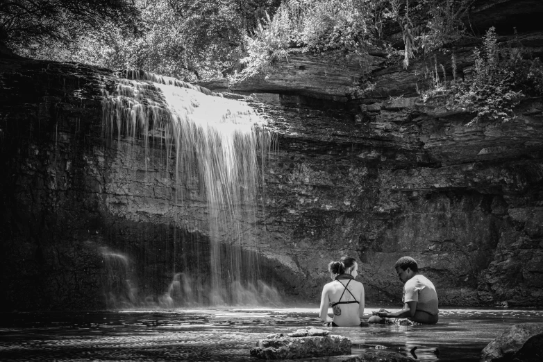 a couple sitting on the rocks near a waterfall