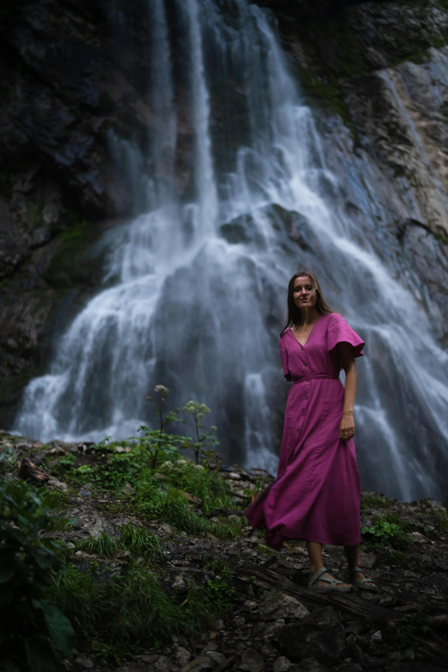 a young woman in pink dress standing in front of water fall