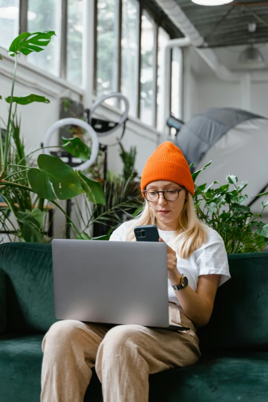 a woman in orange beanie on couch using a laptop computer