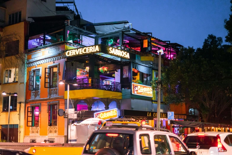 several cars drive by an apartment building with bright neon lights