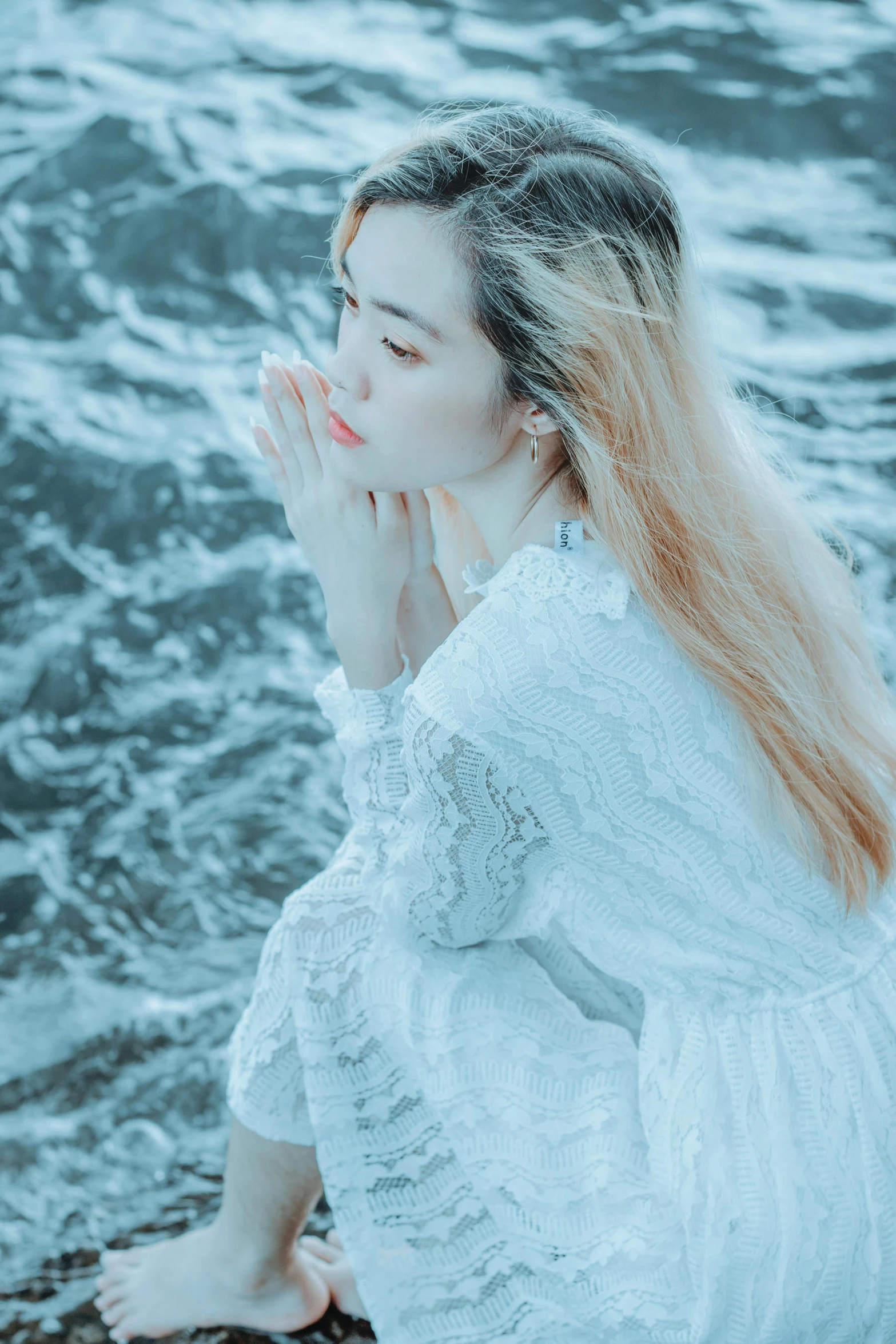 a woman with long hair and white dress sitting on the beach