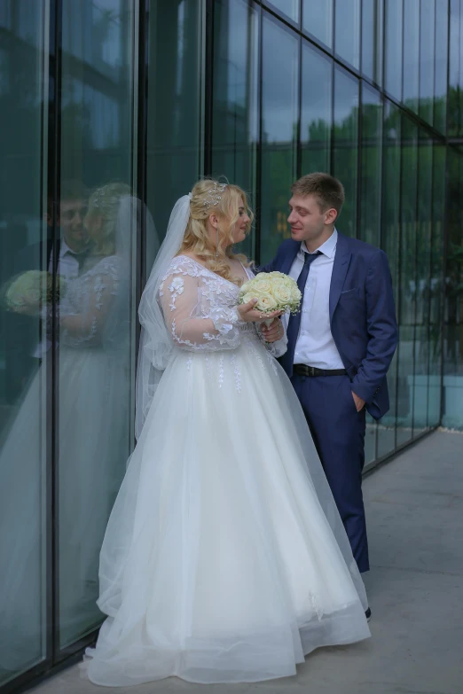 a woman in a wedding dress standing next to a man with a bouquet of flowers