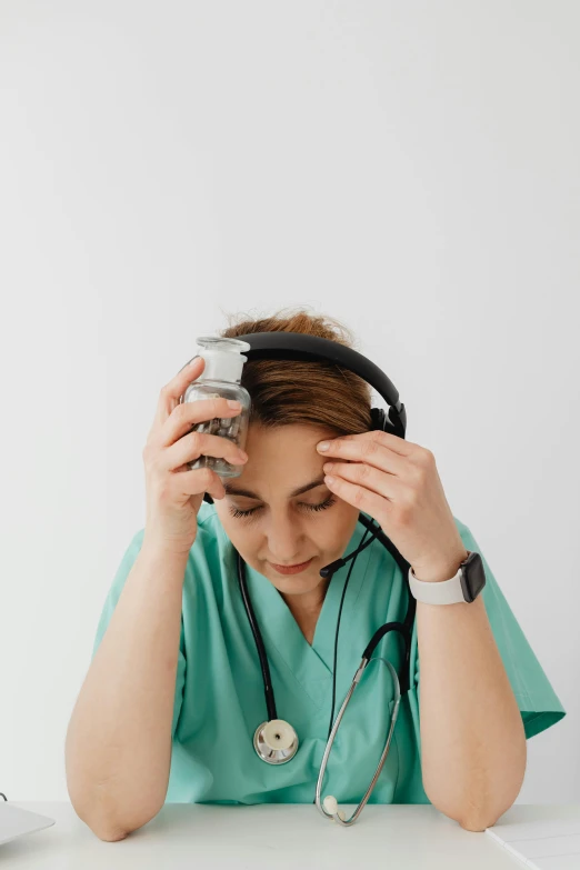 a person in scrubs, holding her head up, wearing a stethoscope and listening to his radio