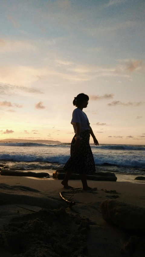 a woman walks on a beach with the sun setting