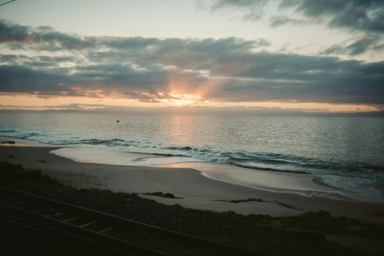 the sun is setting at a beach on a cloudy day