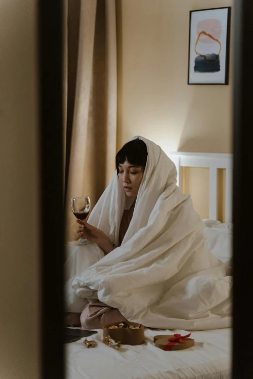 a lady sitting on her bed looking at a glass of wine