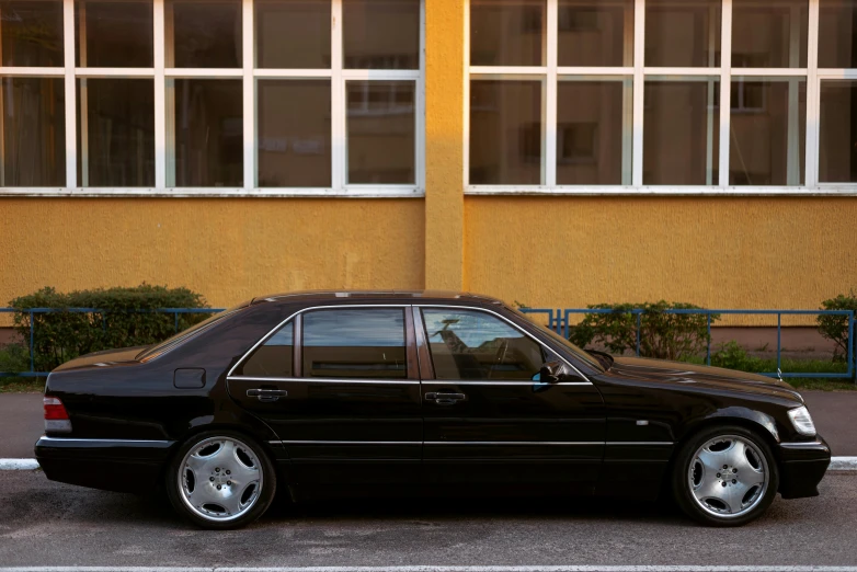 a black mercedes benz car sitting outside a yellow building