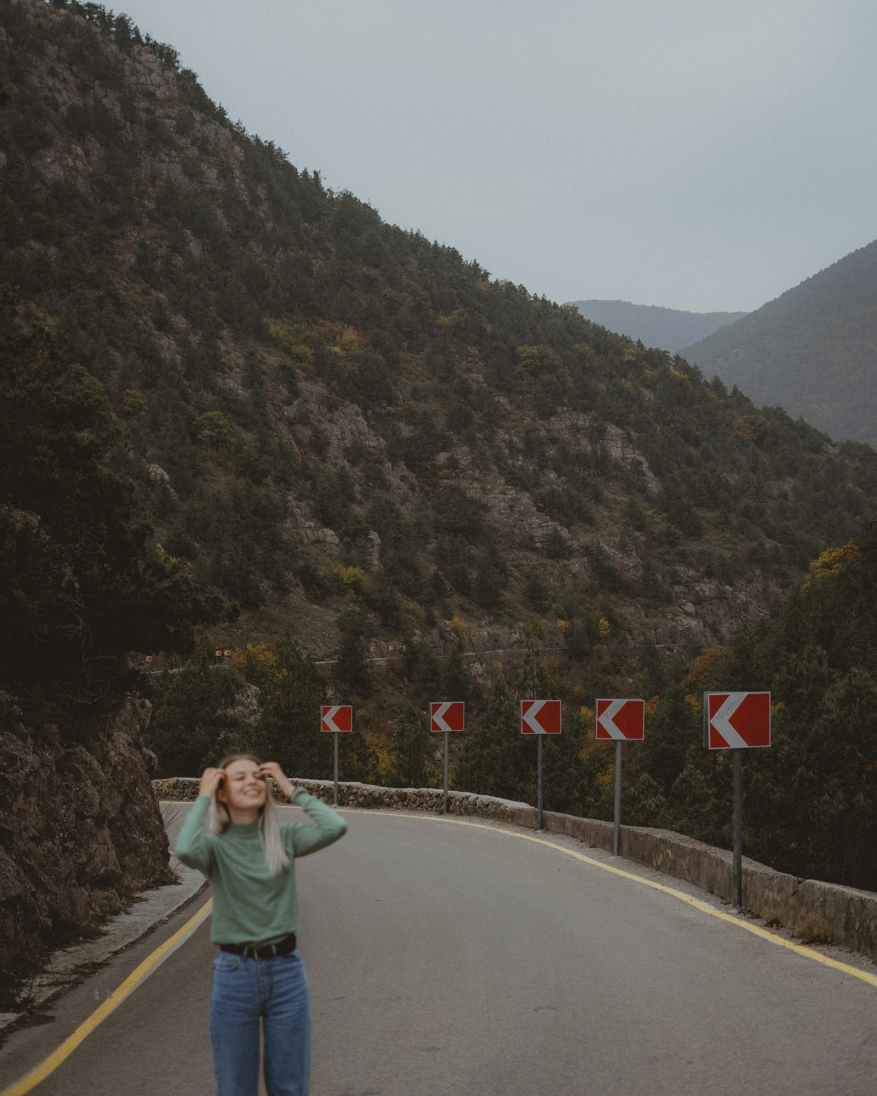 a woman with her hand up to her ear on the side of a road