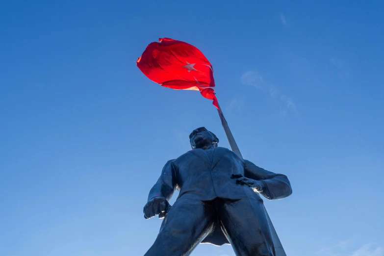 the statue stands under a clear blue sky with a red flag