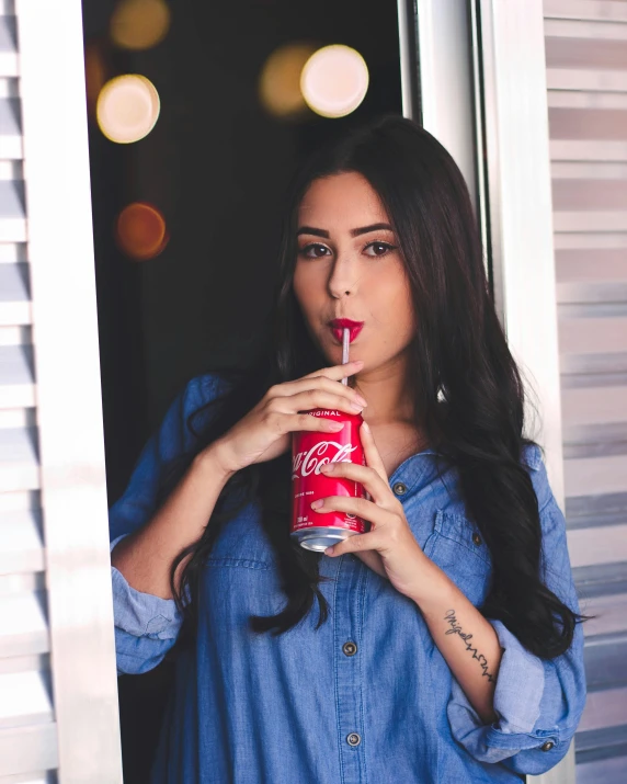 a woman holding a canned beverage in one hand and looking through the window