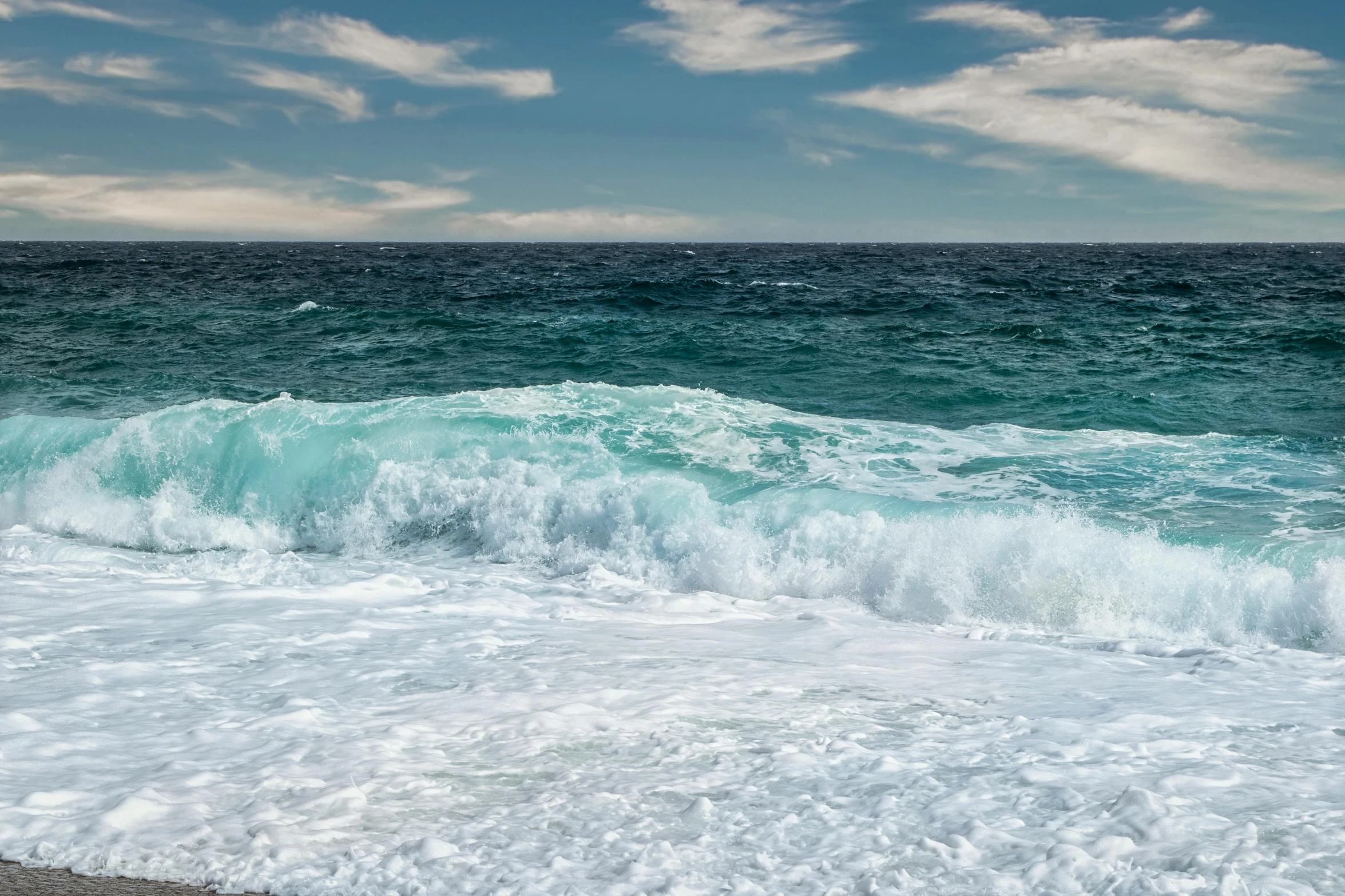 large waves crashing on the beach with white clouds